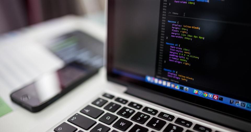 Ecrã de portátil a mostrar código de um site, com um telemóvel desfocado ao lado