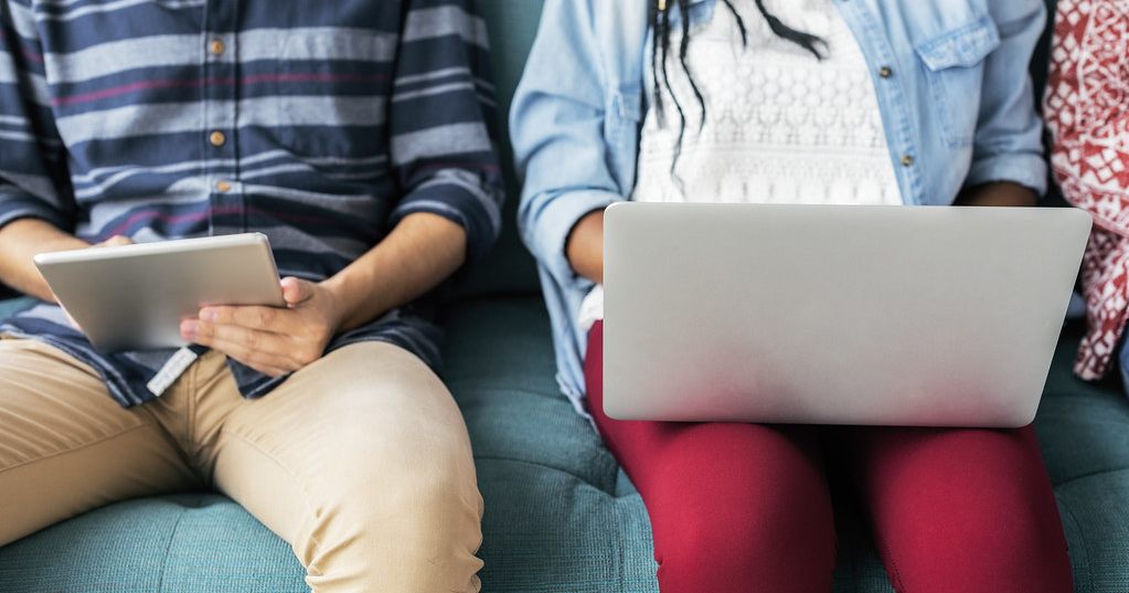 Duas pessoas sentadas num sofá, cada uma a usar um portátil ou tablet